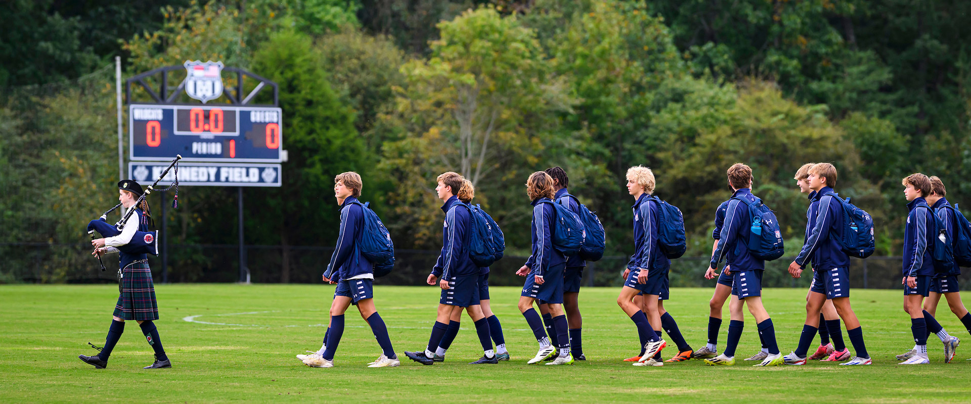 Soccer team walking across field behind bagpiper