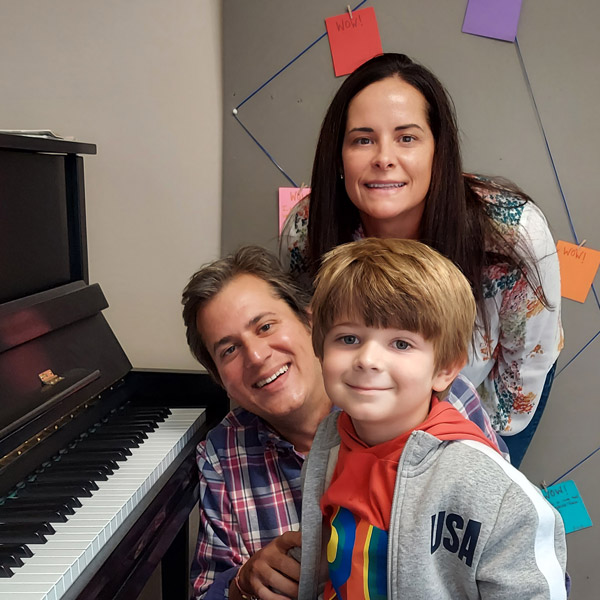 Piano student sitting at piano with his parents